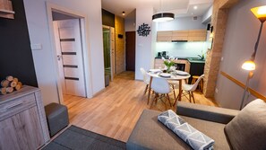 Eine moderne Küche mit Holzschränken, ein Essbereich mit rundem Tisch und Stühlen sowie ein Wohnbereich mit Sofa und Lampe.