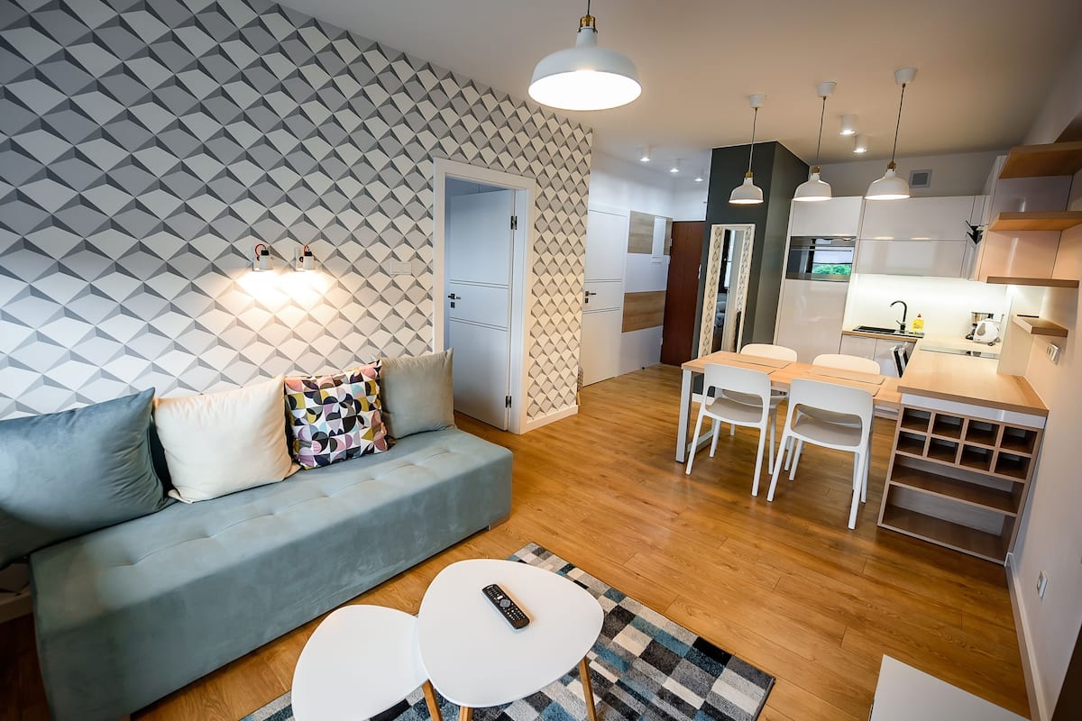 Un salon moderne avec un canapé, deux tables blanches et un mur orné d’un motif.