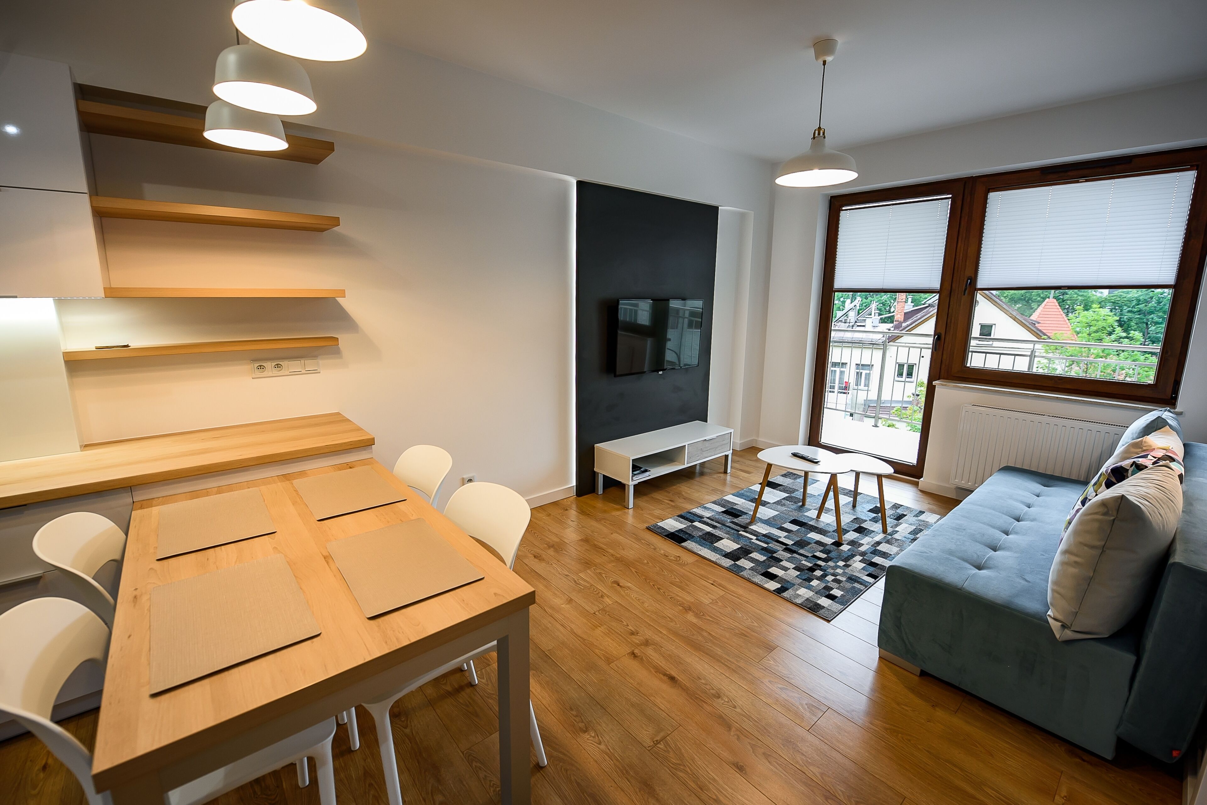 Un espacio de estar moderno con una mesa de comedor de madera, sillas blancas, un sofá gris y un televisor montado en la pared.