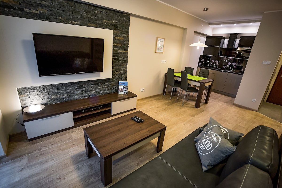 Un salon moderne avec un téléviseur à écran plat, une table basse en bois, un canapé et un coin repas avec une nappe verte.