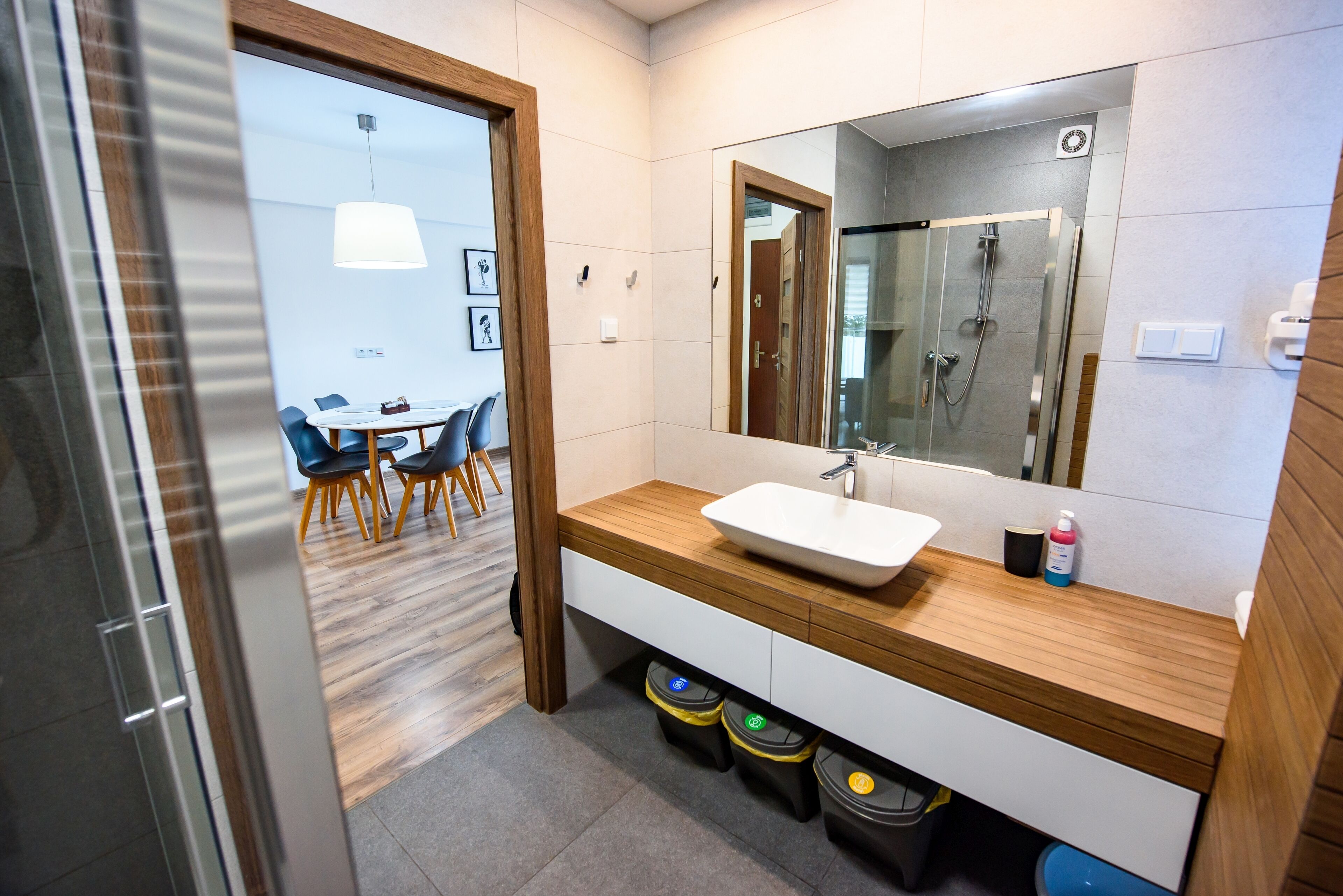 A modern bathroom with a wooden vanity, a large mirror, and a glass shower enclosure.