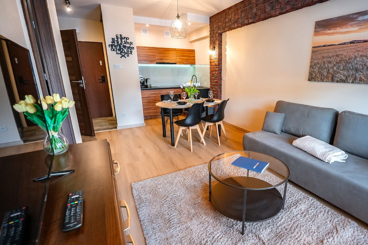 Un salon moderne avec un canapé gris, une table basse et un coin repas avec une table dressée pour quatre personnes.