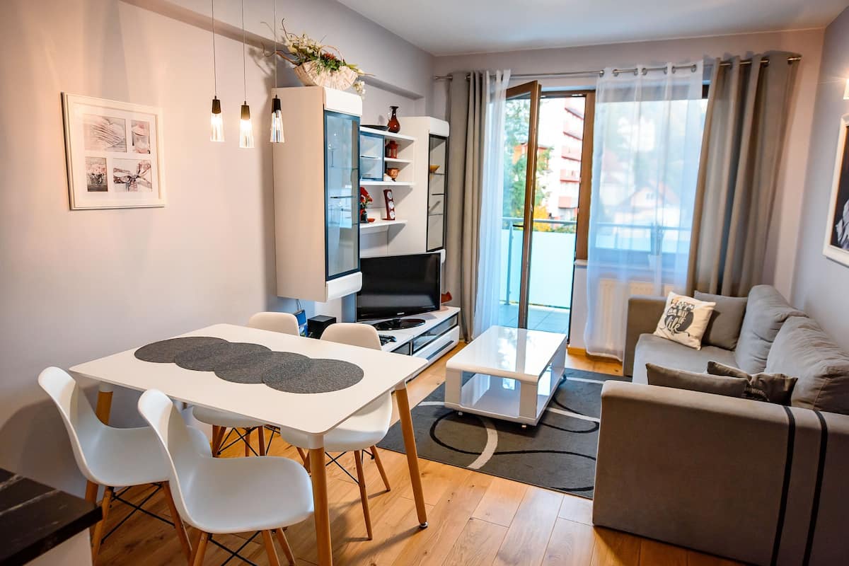 Un salon moderne comprenant un coin repas, un canapé, un téléviseur et un balcon agrémenté de rideaux.
