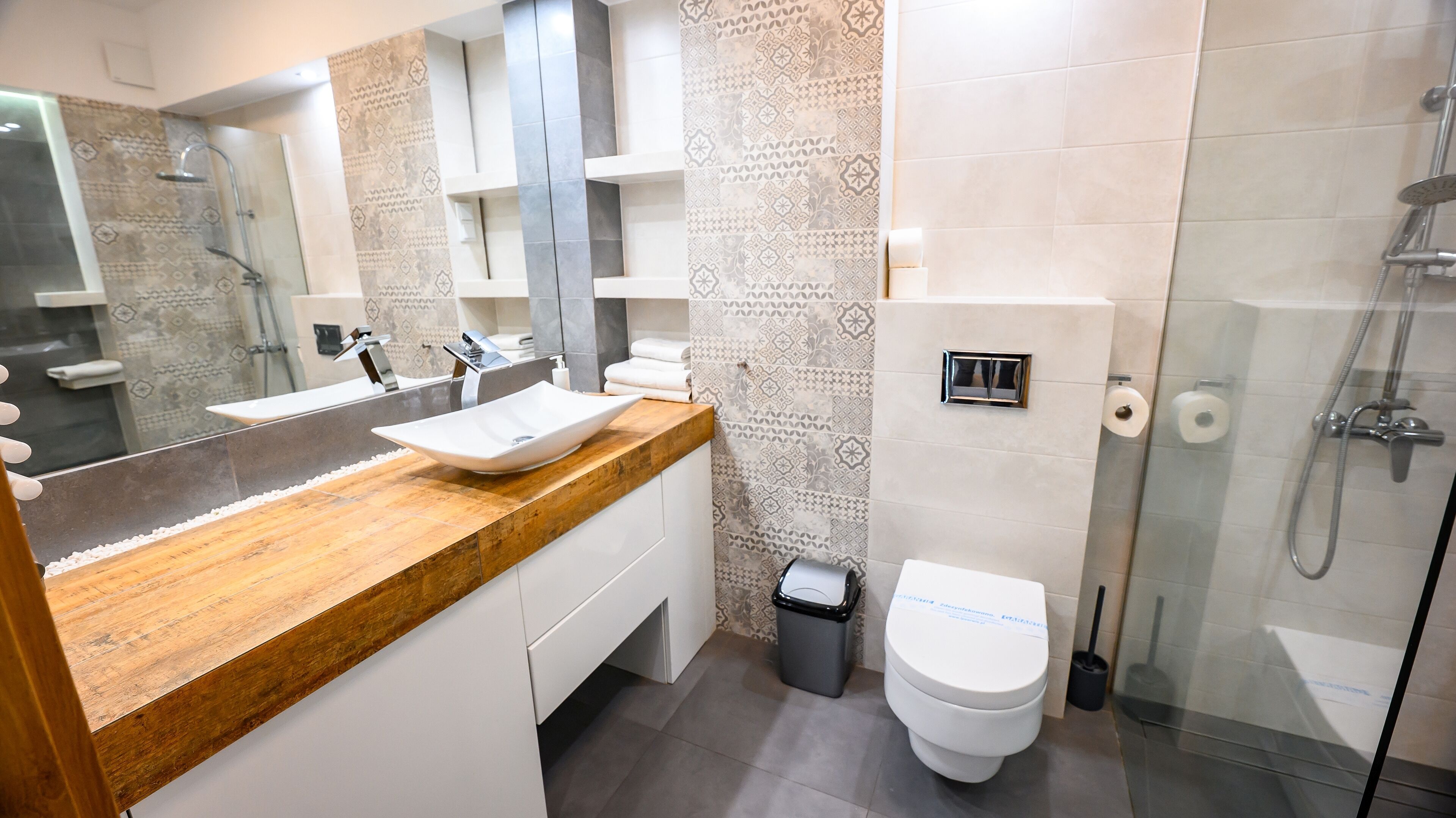 A modern bathroom with a wooden vanity, a white sink, and a glass-enclosed shower.