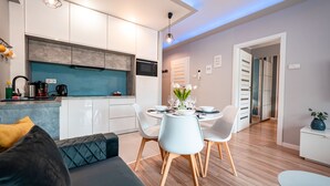 Cozinha moderna com armários brancos, painel de fundo azul e área de jantar com mesa e cadeiras redondas.
