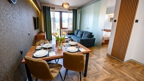 Uma área de jantar com uma mesa de madeira posta para dois, um sofá e uma cama ao fundo.