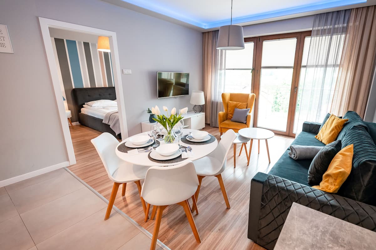 Un salon moderne avec un canapé, une table à manger pour quatre personnes et un téléviseur fixé au mur.