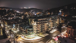 Um hotel com vários andares e varandas, uma rua coberta de neve e edifícios ao redor.