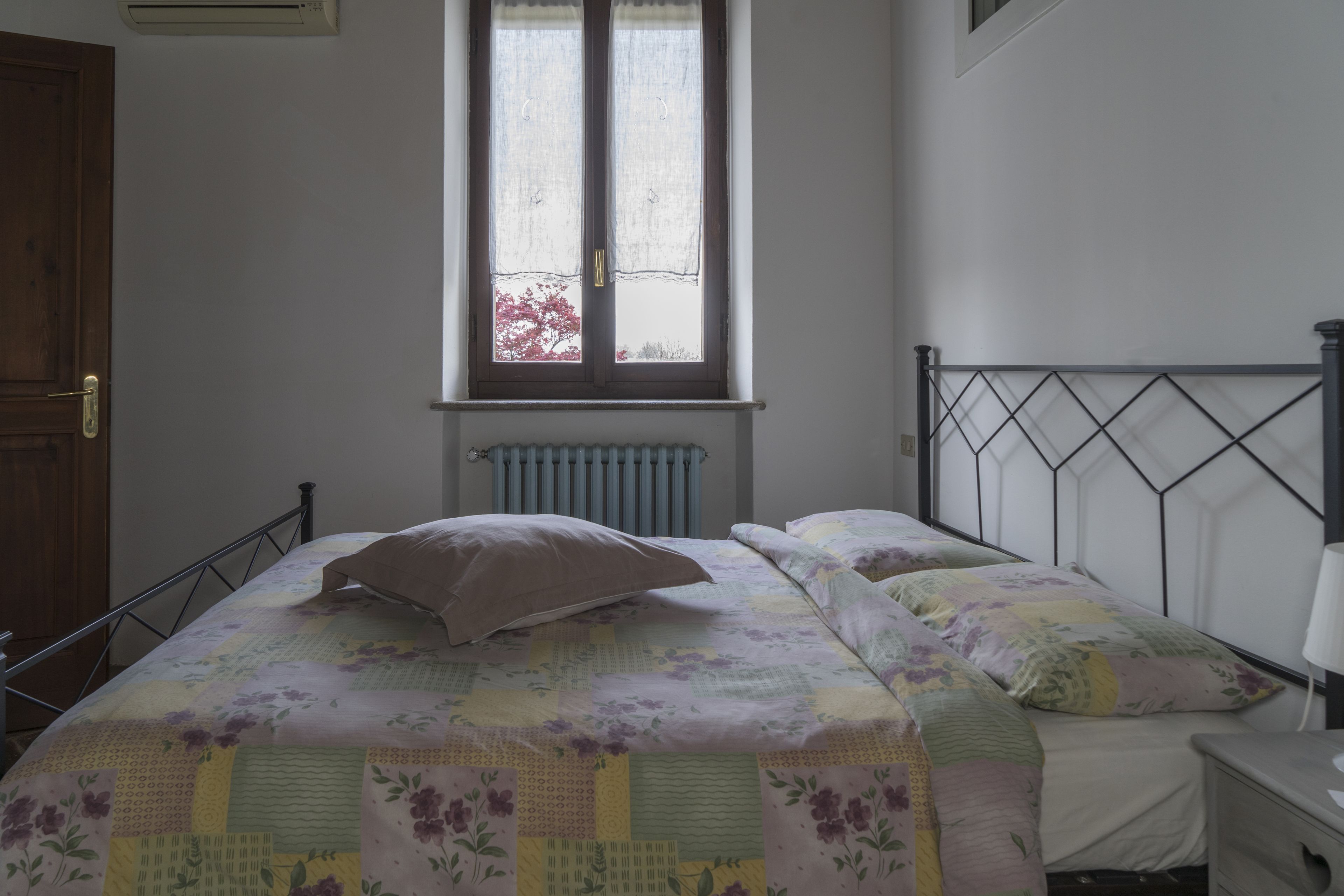 Una camera da letto con un letto, una finestra, un termosifone e un comodino.