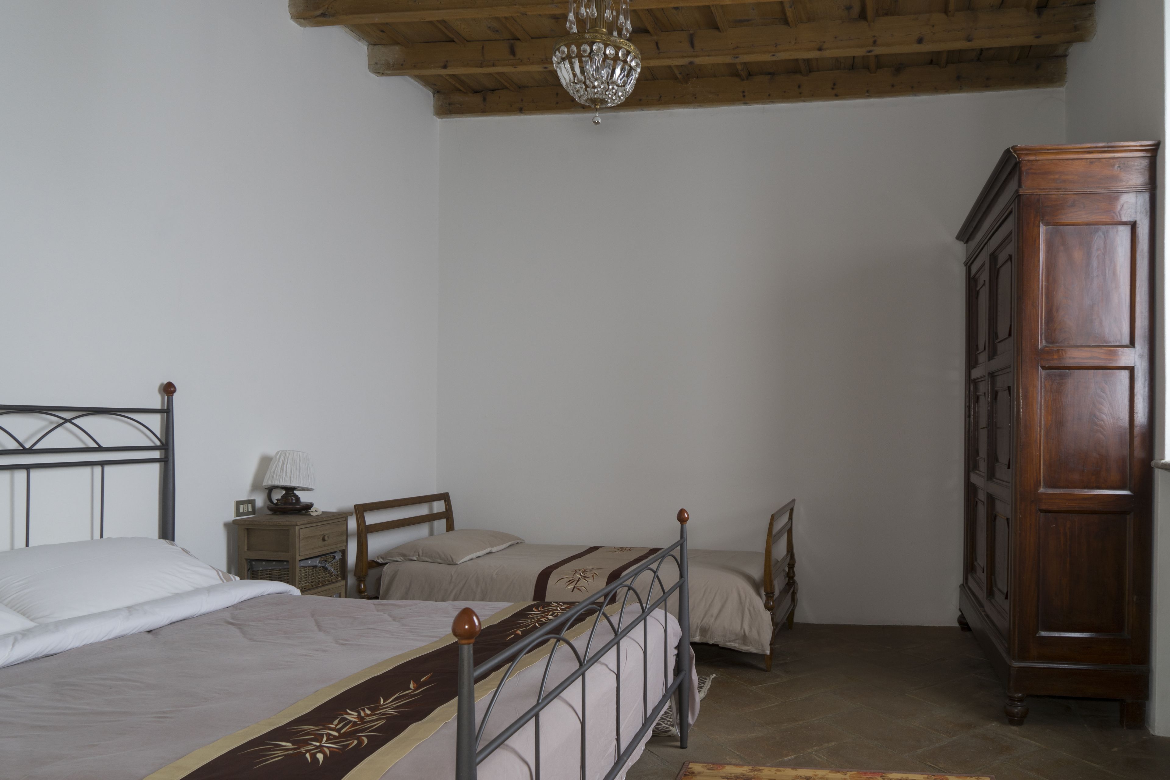 A bedroom with two beds, a wooden wardrobe, a chandelier, and a nightstand with a lamp.