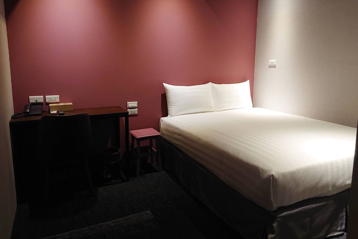 A small hotel room with a bed, a desk, a chair, and a telephone.