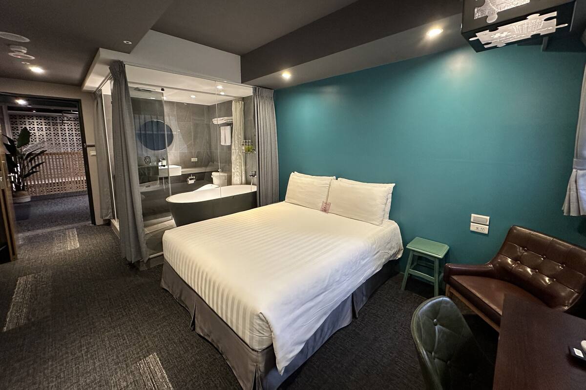 A hotel room with a bed, a bathroom with a bathtub, a desk, and a chair.