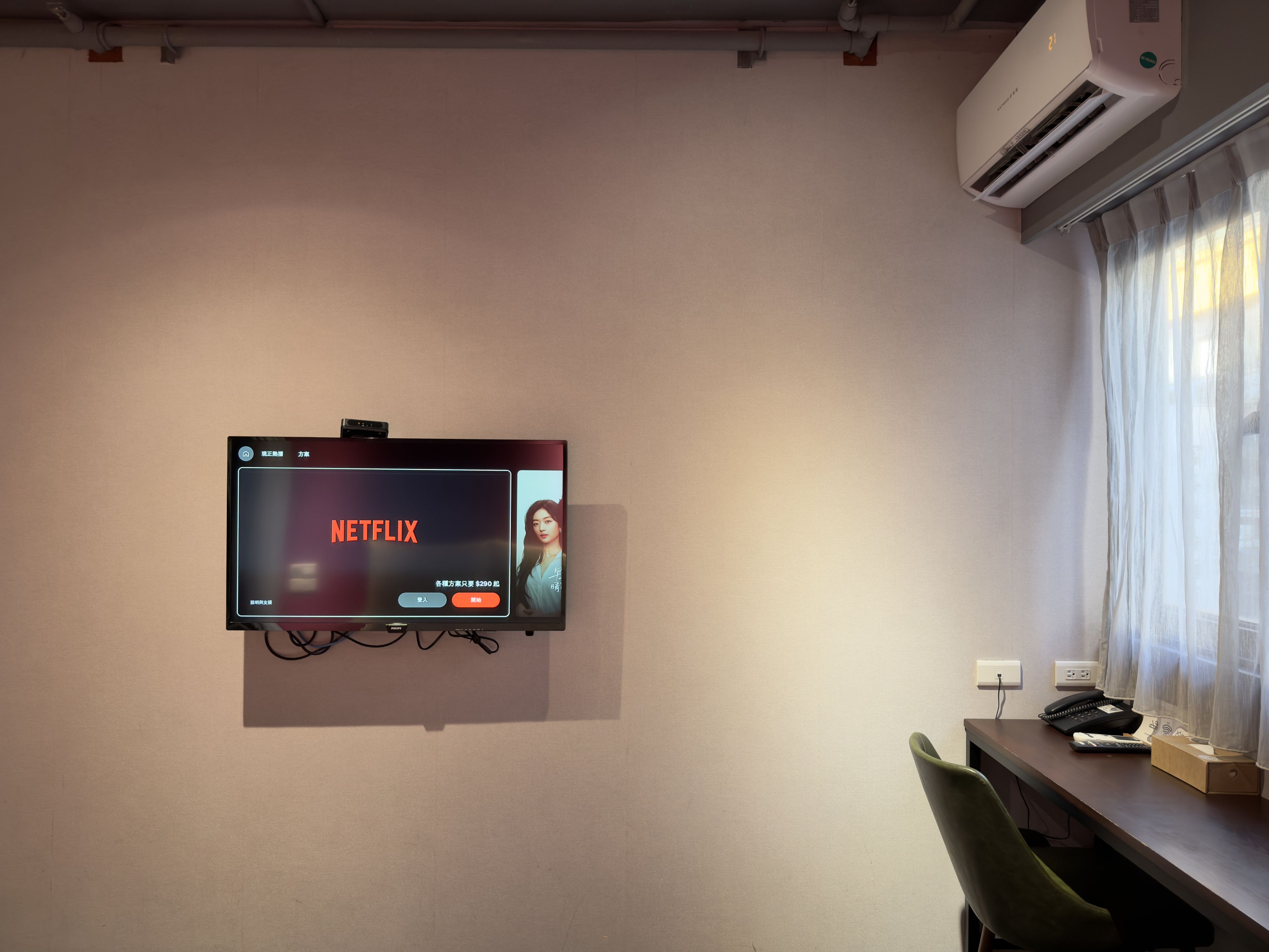 A wall-mounted television displaying the Netflix logo, a desk with a telephone, and a chair.