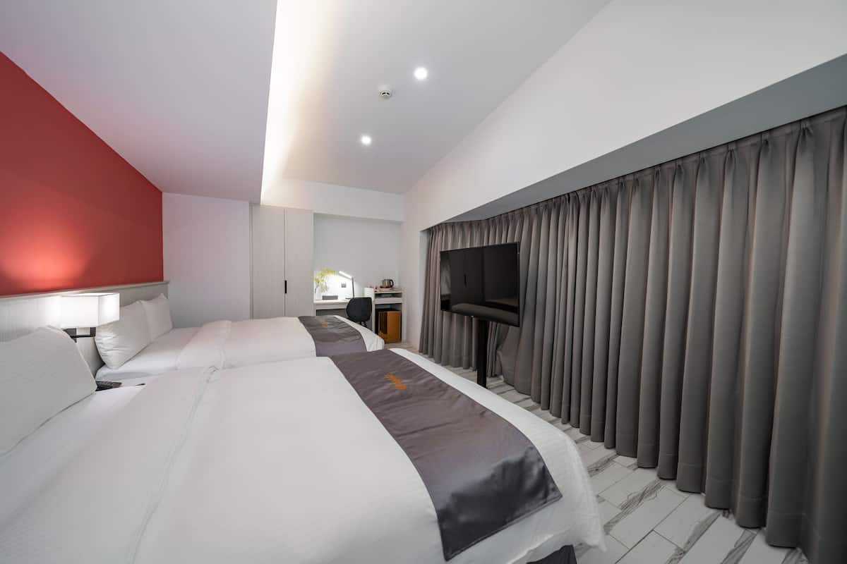 Ein Hotelzimmer mit zwei Betten, einem Schreibtisch, einem Sessel, einem Fernseher und einem großen Fenster mit Vorhängen.