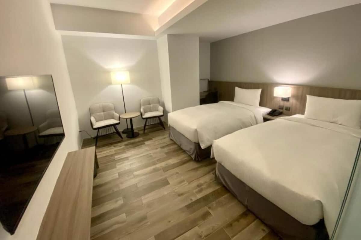 Ein Hotelzimmer mit zwei Betten, einer Sitzecke mit Stühlen, einem kleinen Tisch und einer Lampe.