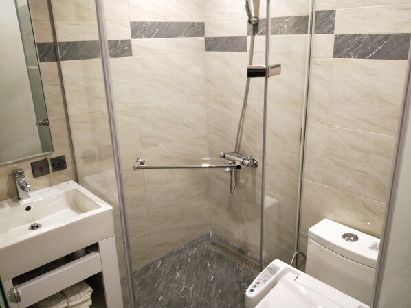 A glass-enclosed shower with a handheld showerhead, a handheld shower attachment, and a control panel.