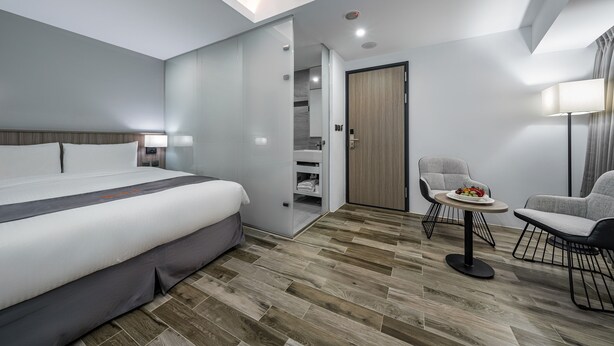 Ein modernes Hotelzimmer mit einem großen Bett, einem kleinen Esstisch, zwei Stühlen, einem Kleiderschrank und einer Deckenleuchte.