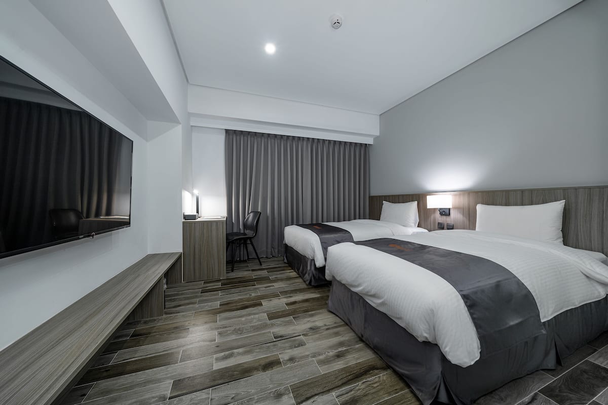 Ein modernes Hotelzimmer mit zwei Betten, einem Schreibtisch, einem Stuhl und einem großen Spiegel.