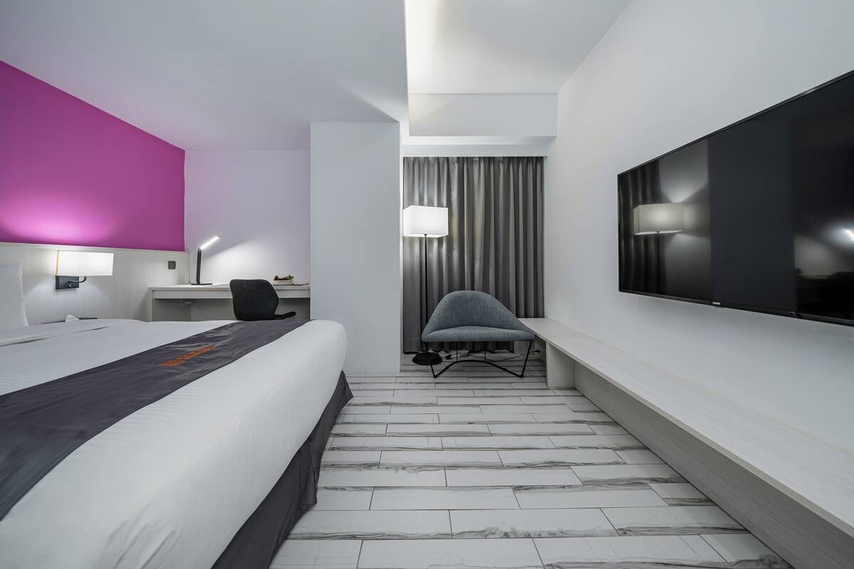 Ein modernes Hotelzimmer mit einem großen Bett, einem Schreibtisch, einem Stuhl, einem Fernseher und einem Vorhang.