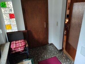 Una habitación con puerta de madera, una silla con cojín escocés, una mesita y un ventanal con vidrios de colores.