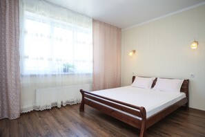 A bedroom with a wooden bed, a window with sheer curtains, and a radiator. - Apartment Inessa 34 (Odesa)
