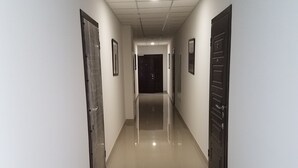Un long couloir étroit, doté d’un sol carrelé brillant et de murs blancs. Des portes se trouvent de part et d’autre du couloir, et on aperçoit un luminaire au plafond.