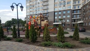 Une aire de jeux avec des structures d’escalade et un banc, entourée de petits arbres et d’une zone pavée.