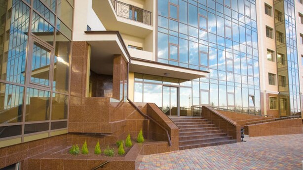Un bâtiment moderne doté d’une façade en verre, d’une entrée centrale avec un espace abrité et d’un escalier menant à l’entrée.