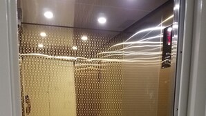 Un ascenseur à l’intérieur métallique, avec un panneau de commande sur le côté droit et un sol à motifs.
