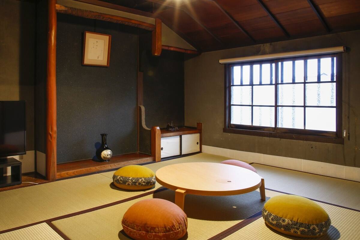 Een kamer met tatami matten, een tatami tafel, kussens, een klein kastje en een raam met uitzicht.