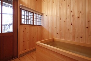 Une pièce en bois avec une grande baignoire, une fenêtre grillagée et un plancher en bois.