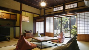 A traditional Japanese room with tatami flooring, a low table, cushions, and sliding doors leading to a garden. - Yamasaki Ryokan Q Nakamonzenya (Shiso)
