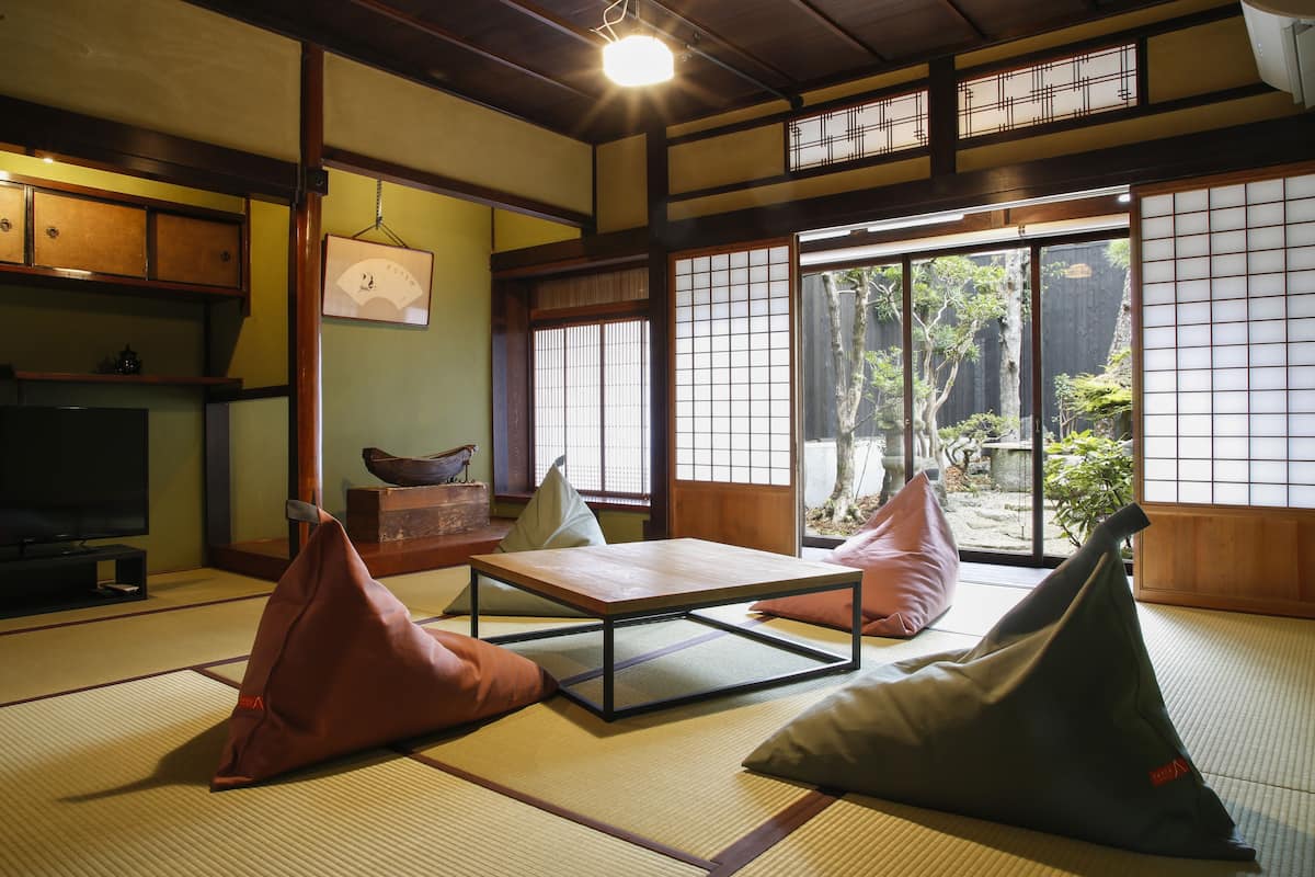 Een traditionele Japanse kamer met tatami vloerbedekking, een lage tafel, kussens en schuifdeuren die uitkomen op een tuin.