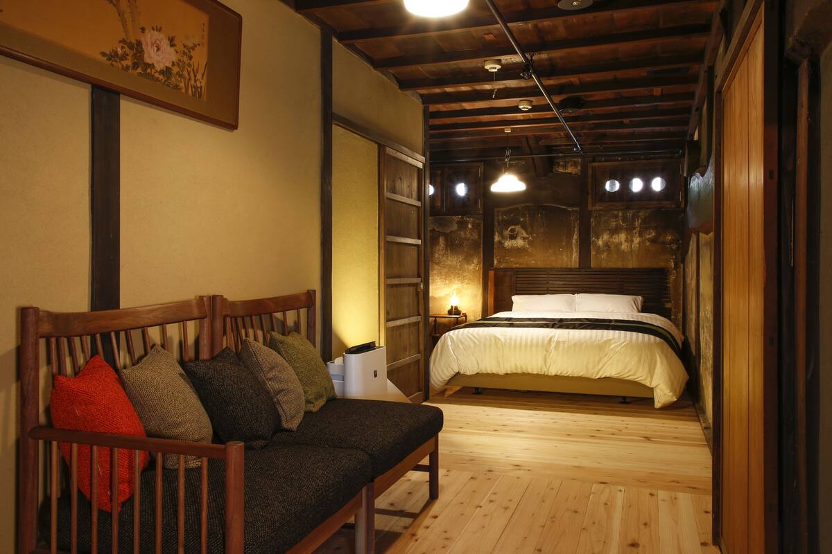 Een gezellige kamer met een houten bank, een bed met wit beddengoed en een houten plafond.