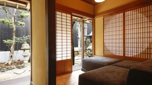 A traditional Japanese room with tatami flooring, a low wooden bed, sliding doors, and a view of a garden with a tree and stone lantern. - Yamasaki Ryokan Q Nakamonzenya (Shiso)