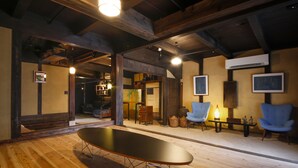 A spacious room with wooden flooring, a long table, two blue armchairs, and a ceiling with exposed beams. - Yamasaki Ryokan Q Nakamonzenya (Shiso)