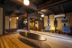 A spacious room with wooden flooring, a long table, two blue armchairs, and a ceiling with exposed beams.