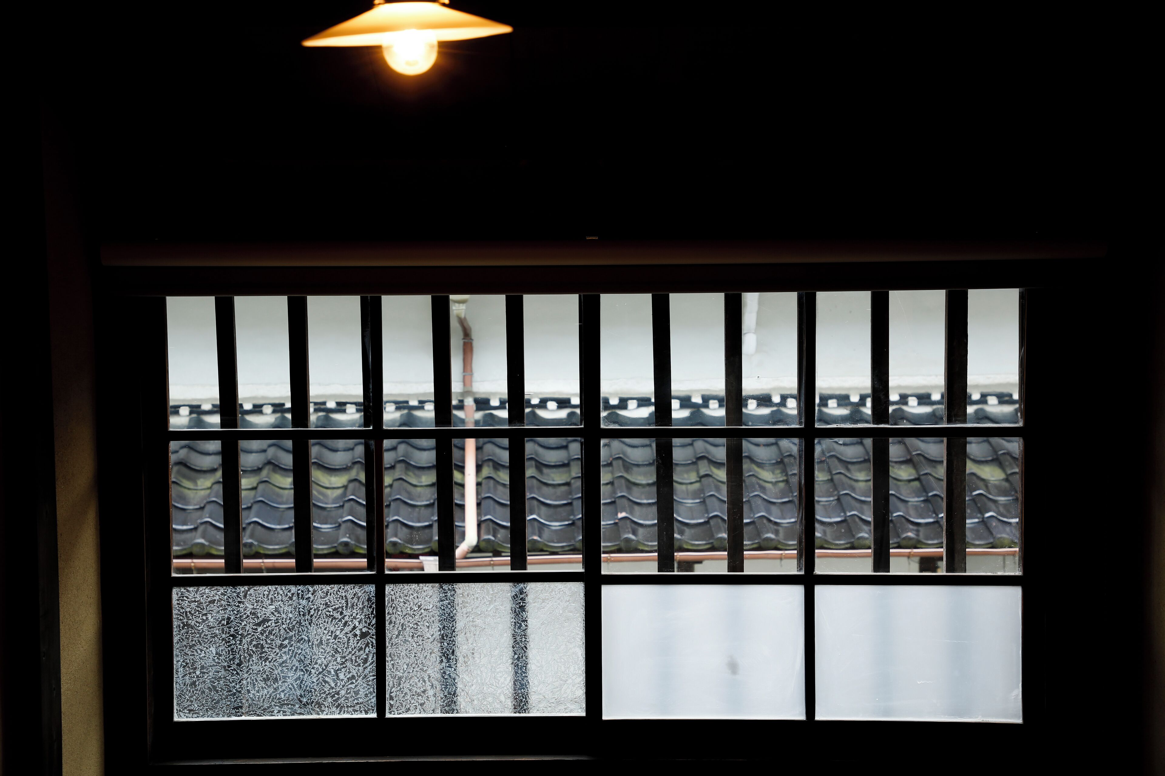 A window with a view of a traditional tiled roof and a partially visible building.