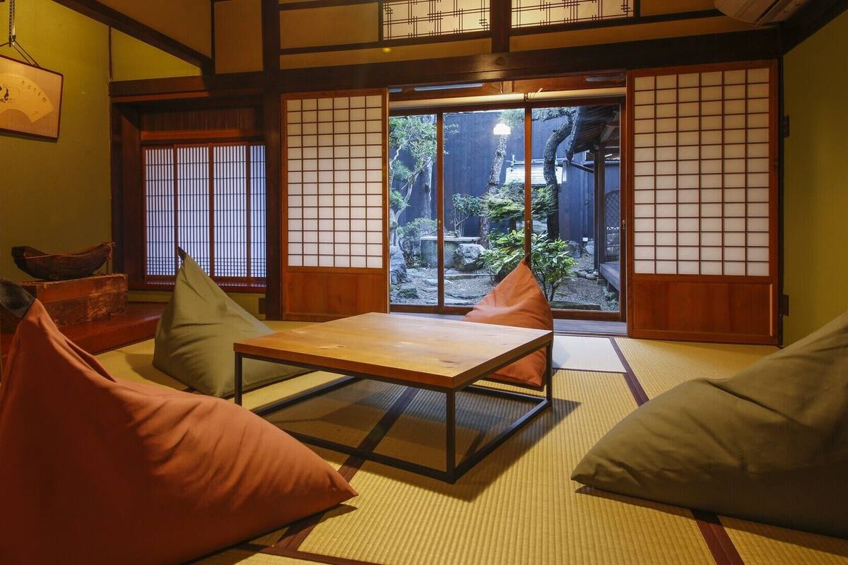 Een traditionele Japanse kamer met tatami vloerbedekking, een lage tafel, kussens en schuifdeuren die uitkomen op een tuin.