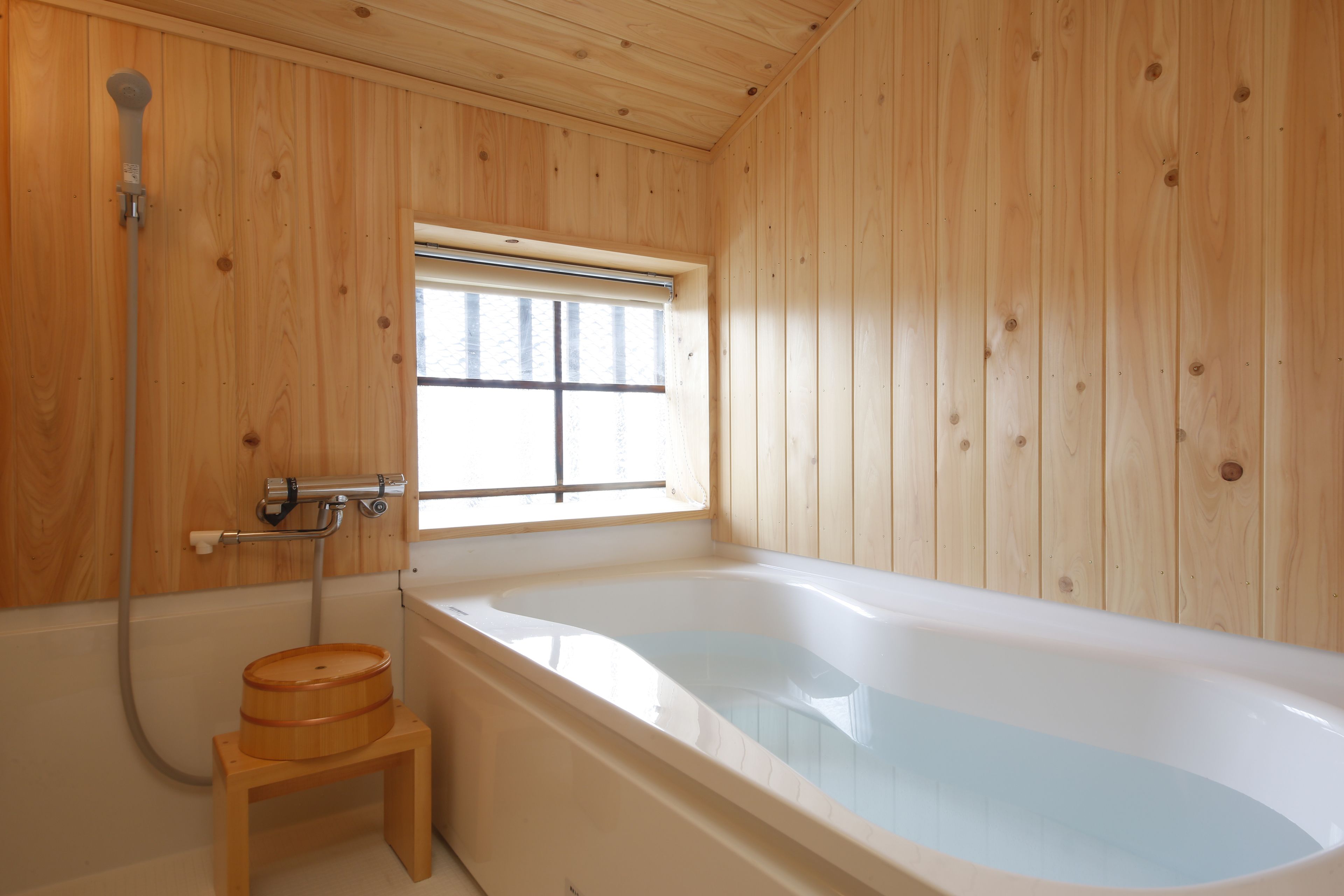 A wooden-paneled bathroom with a bathtub, a wooden stool, and a window.