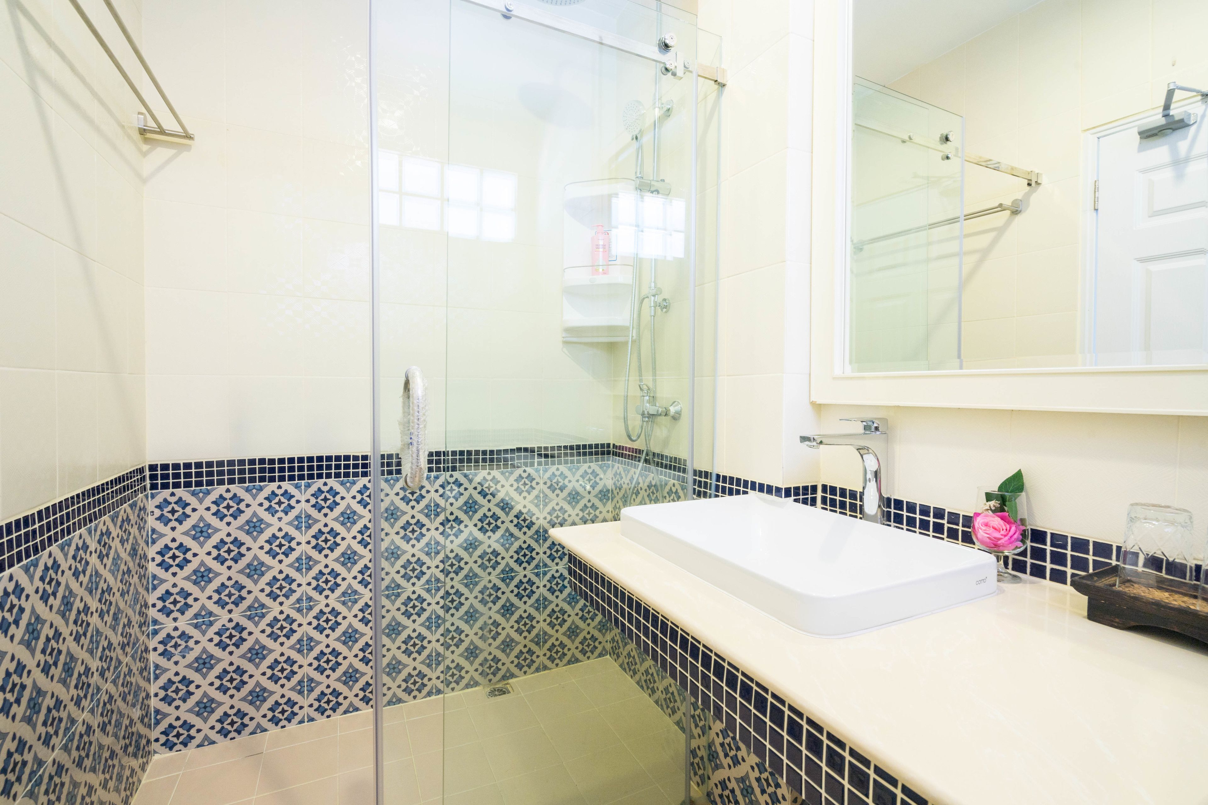 A bathroom with a glass shower enclosure, a white sink, and blue patterned tiles.