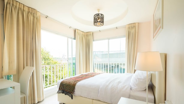 A hotel room with a bed, a desk, a lamp, and large windows with curtains. - Baan Anodat (Nonthaburi)