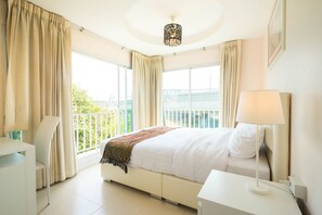 A hotel room with a bed, a desk, a lamp, and large windows with curtains. - Baan Anodat (Nonthaburi)
