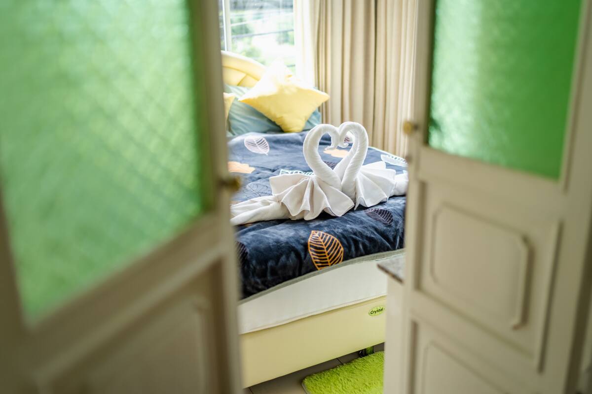 Hotellihuone, jossa on sängyllä sydämenmuotoinen pyyhekoriste ja lehtikuviollinen tyyny.