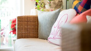 A wicker sofa with a grey cushion and a white pillow with pink text. - Baan Anodat (Nonthaburi)