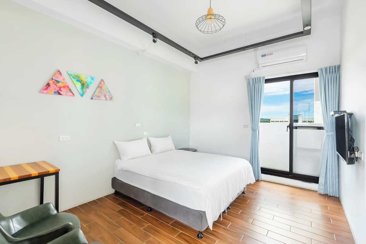 Un dormitorio con una cama, un escritorio, una silla, un televisor y una ventana con cortinas.