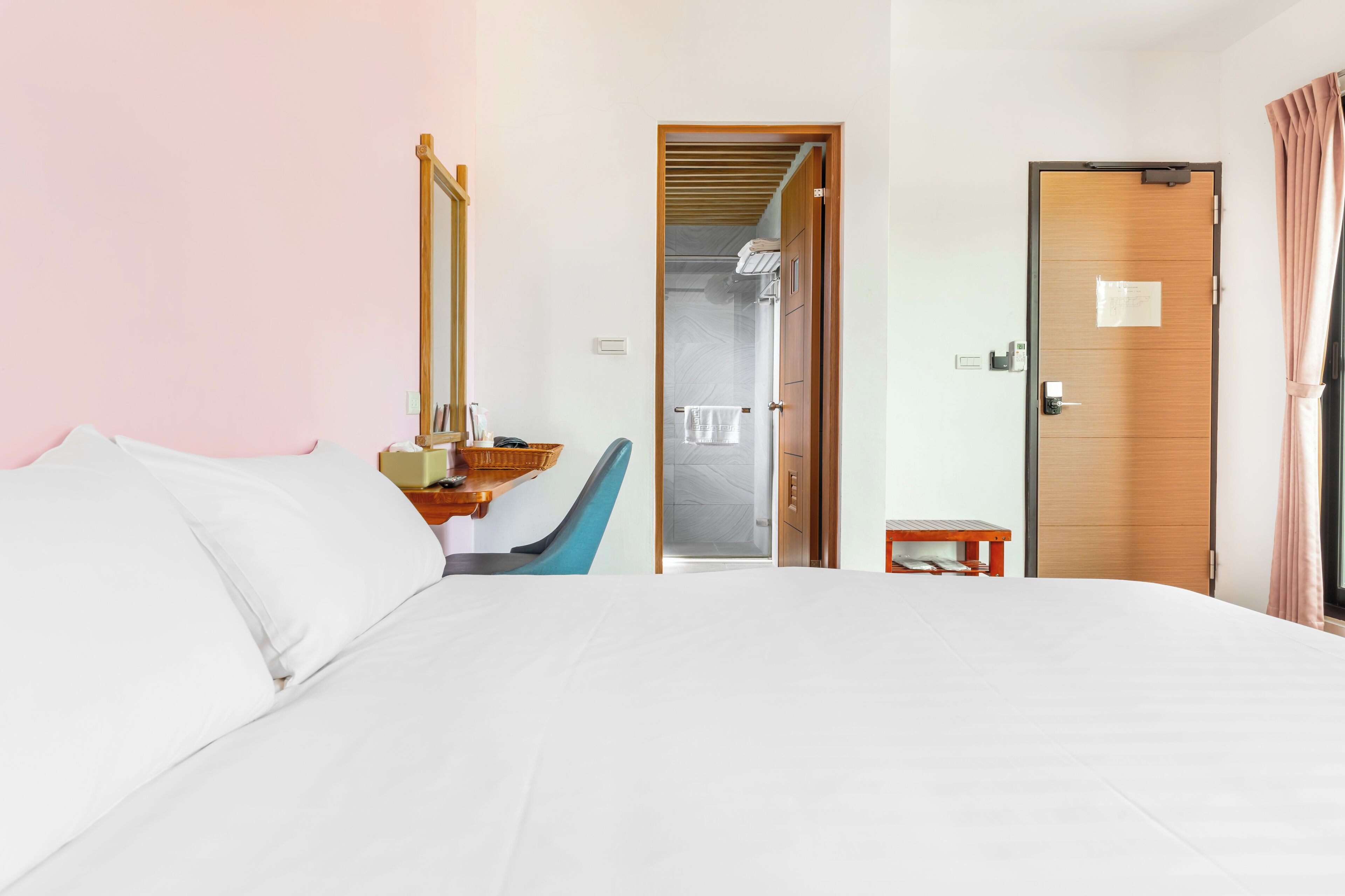 A hotel room with a bed, a mirror, a chair, a small table, and a door leading to a bathroom.