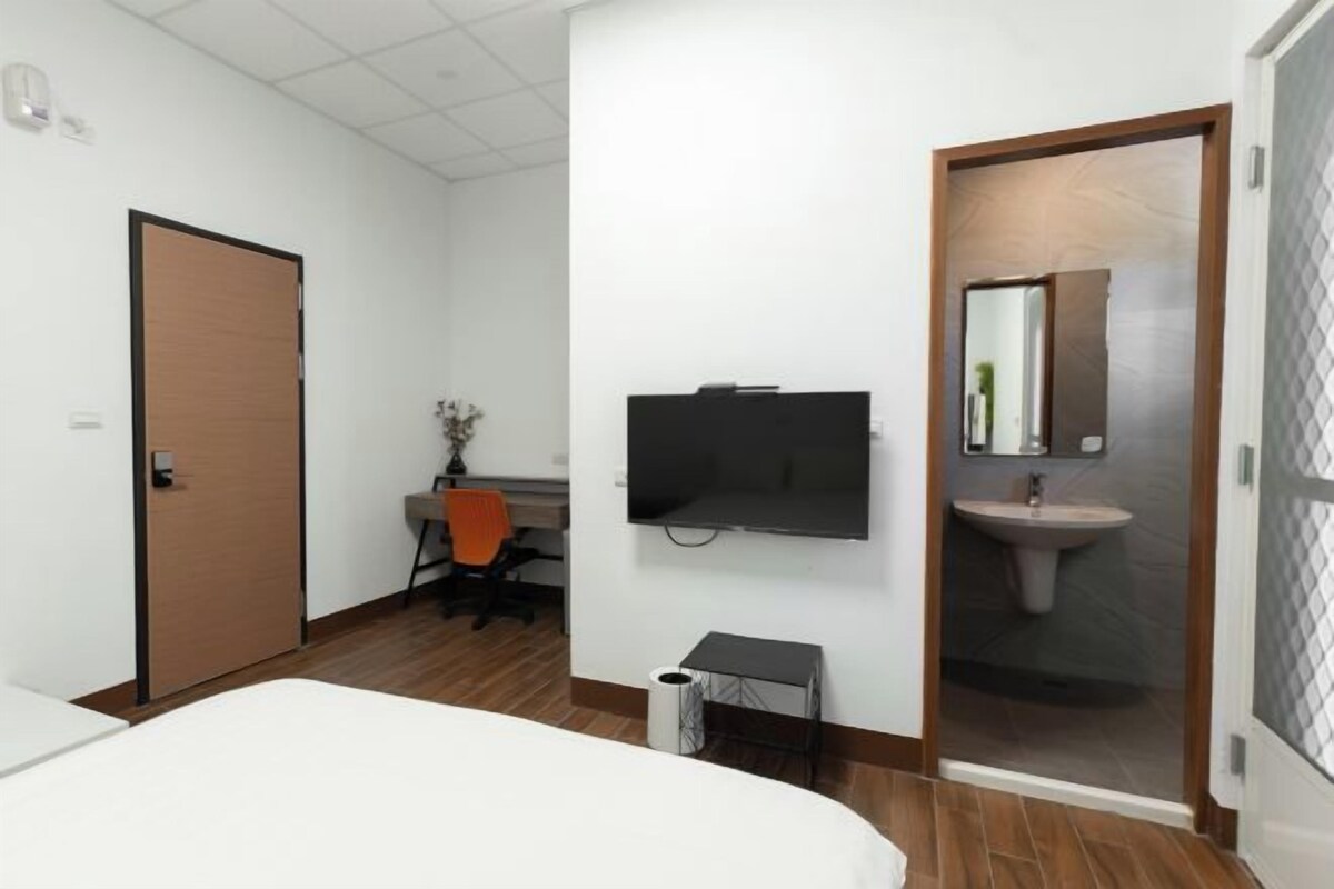 Habitación de hotel con una cama, un escritorio con silla, televisión, lavamanos y una puerta.