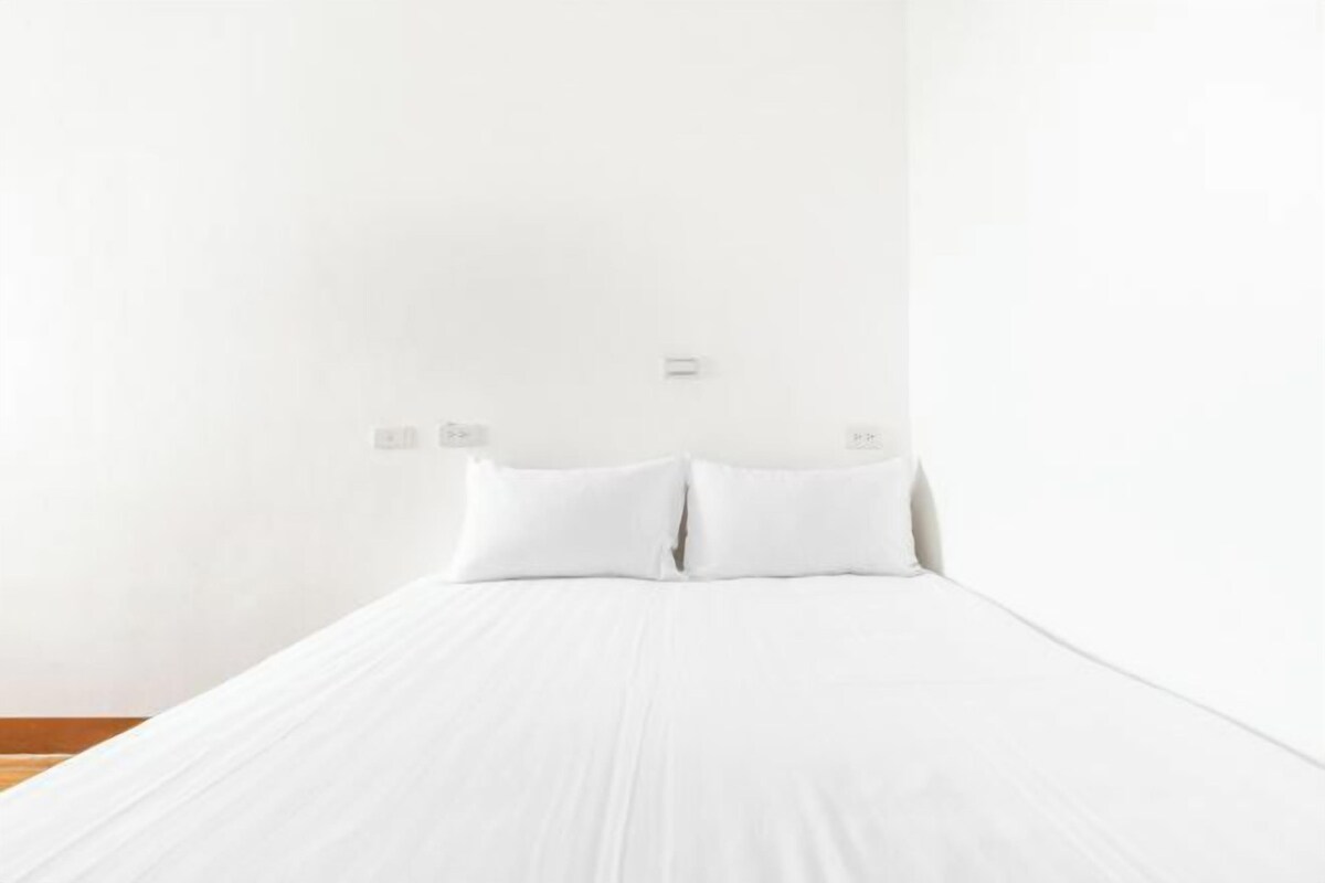 Habitación de hotel minimalista con una cama individual, ropa de cama blanca y una pared lisa de color blanco.