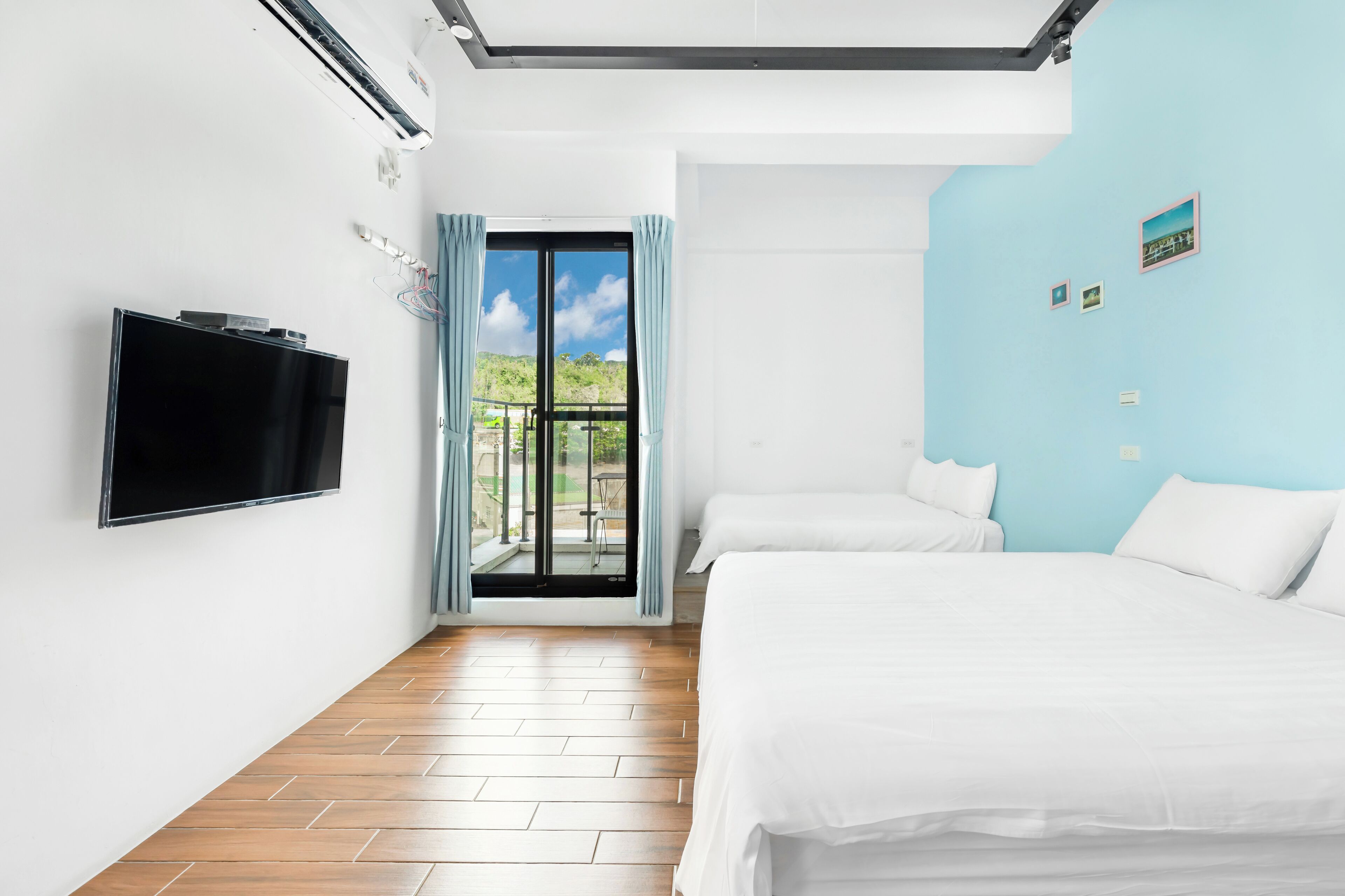 Habitación de hotel con televisión, dos camas, balcón con vistas y ventilador de techo.